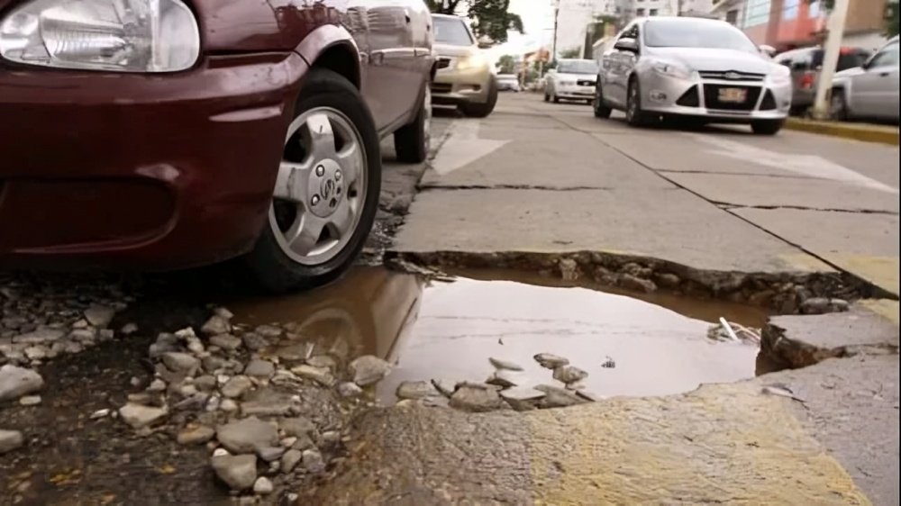 Conductor reduciendo la velocidad de su auto frente a un bache para evitar daños en la suspensión