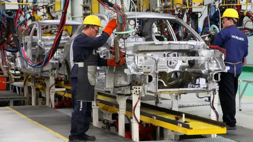Vista general de una planta de producción automotriz con vehículos en la línea de montaje y trabajadores realizando tareas de fabricación