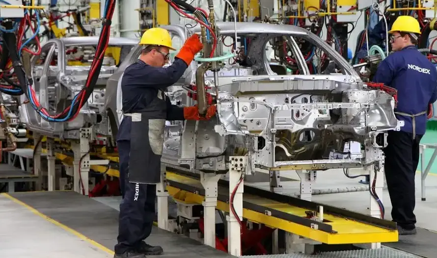 Vista general de una planta de producción automotriz con vehículos en la línea de montaje y trabajadores realizando tareas de fabricación