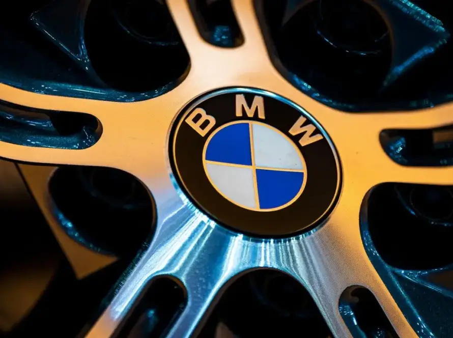 BMW M3 2027, vista frontal, mostrando un diseño deportivo y futurista, destacando sus luces LED y su parrilla distintiva, con un fondo urbano difuminado que sugiere velocidad.