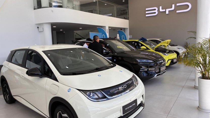 Personas observando un carro eléctrico en una exposición automotriz en Ecuador, con gráficos de crecimiento de ventas al fondo