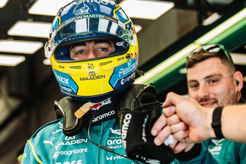 El piloto Fernando Alonso junto a su monoplaza Aston Martin reflexionando en los boxes sobre el reglamento técnico.