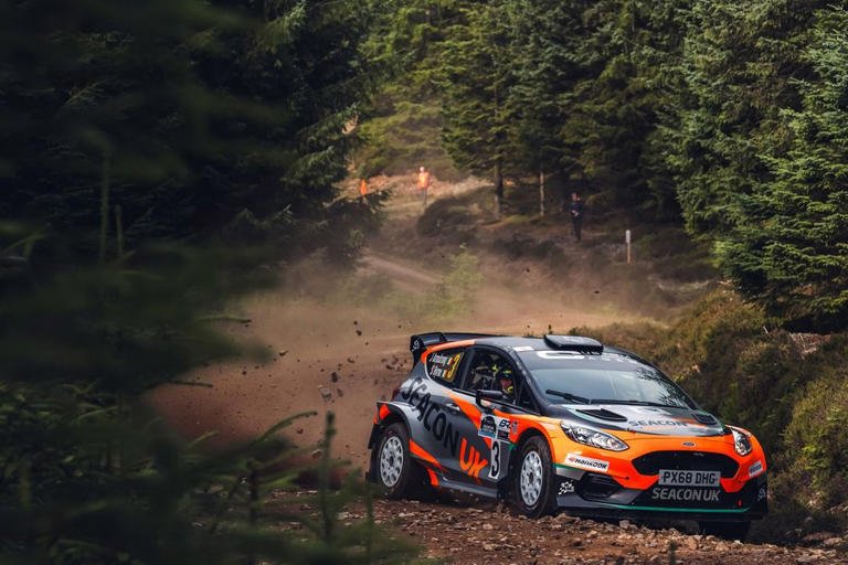 Vista de los tramos de grava y bosques del recorrido del Rally de Escocia del WRC, con infraestructura de asistencia y paisaje escocés de fondo.